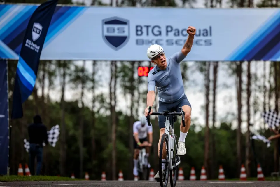 Flavio Secolin pedala ao cruzar a linha de chegada, com um braço erguido.